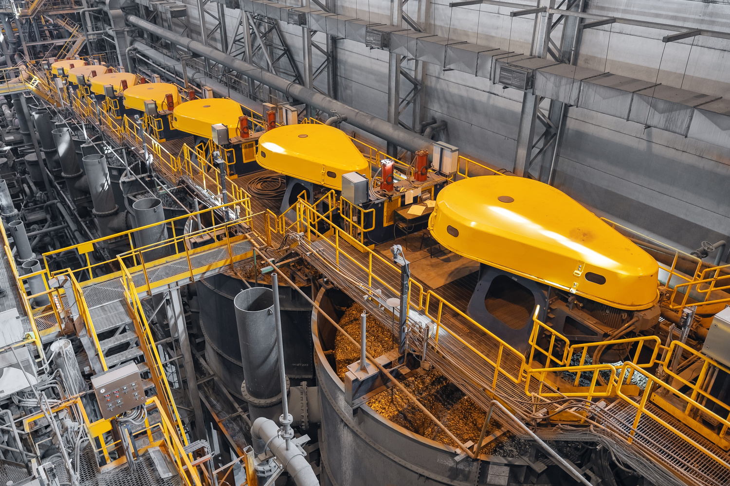 A bank of flotation cells with yellow drive covers, pipework and walkways extending through a mineral processing plant